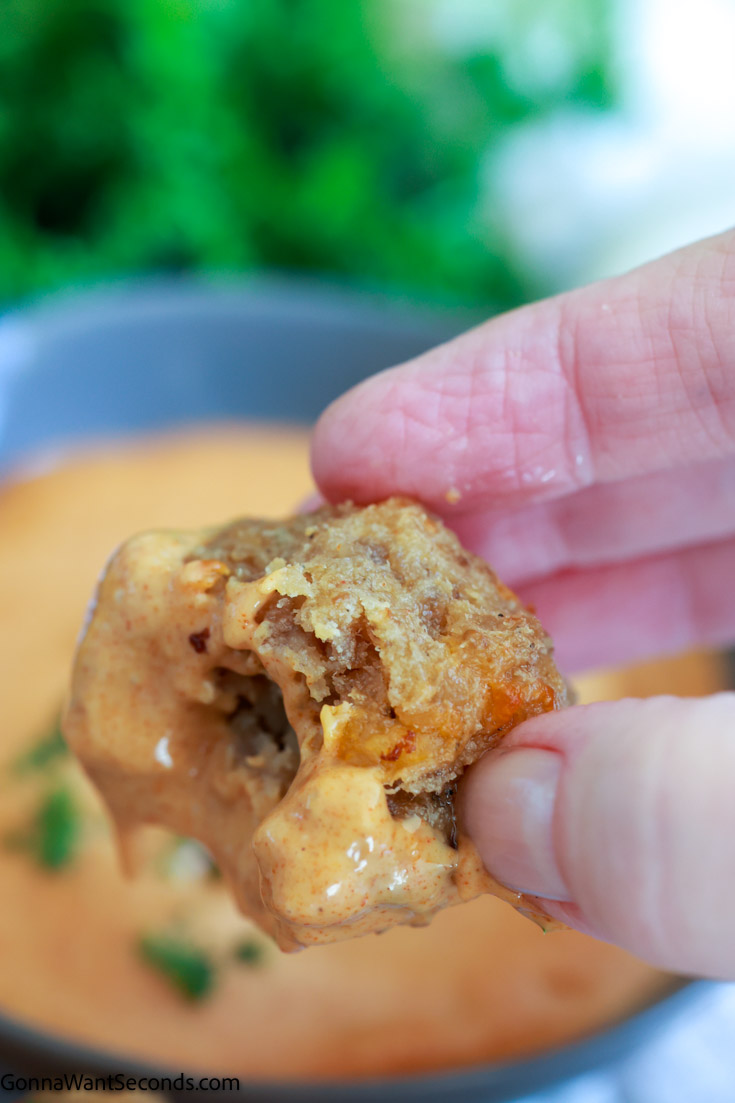 hand holding a bisquick sausage balls with cream cheese dipped in awesome sauce