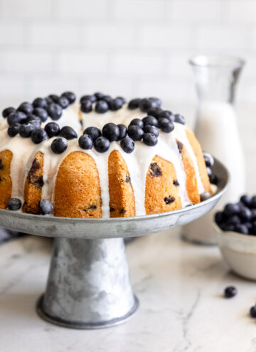 blueberry pound cake with glaze topped with fresh blueberries, on a metal cake stand
