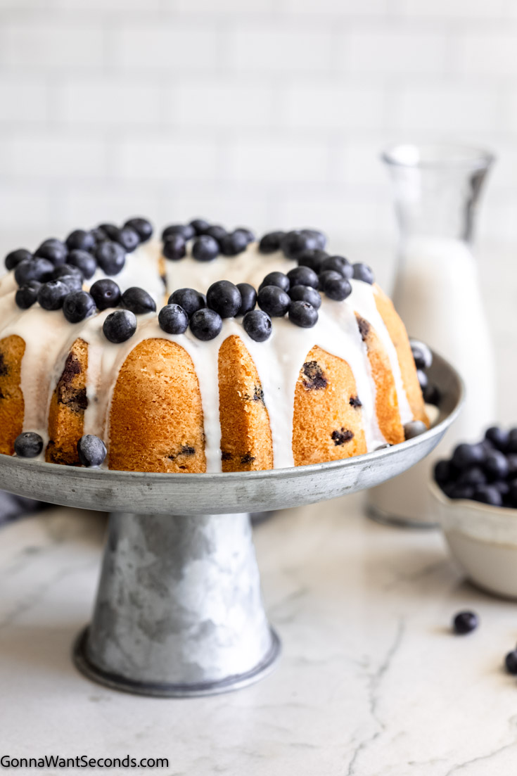 blueberry pound cake with glaze topped with fresh blueberries, on a metal cake stand 