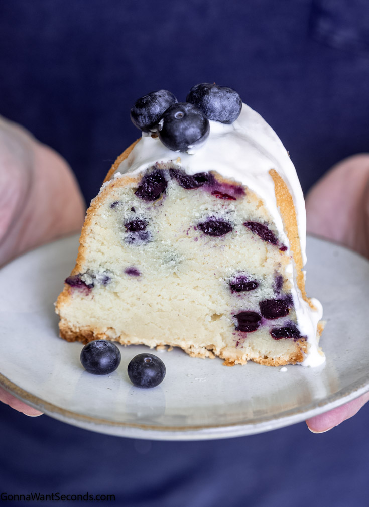 holding a saucer with sour cream blueberry pound cake with glaze topped with fresh blueberries