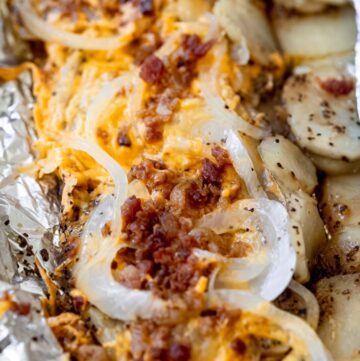 simple campfire potatoes topped with cheese, onion, and bacon, in aluminum foil