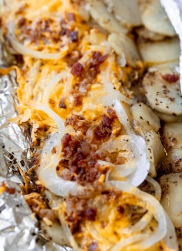 simple campfire potatoes topped with cheese, onion, and bacon, in aluminum foil