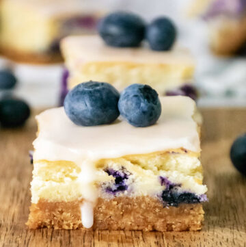 a slice of blueberry cheesecake bars topped with fresh blueberries
