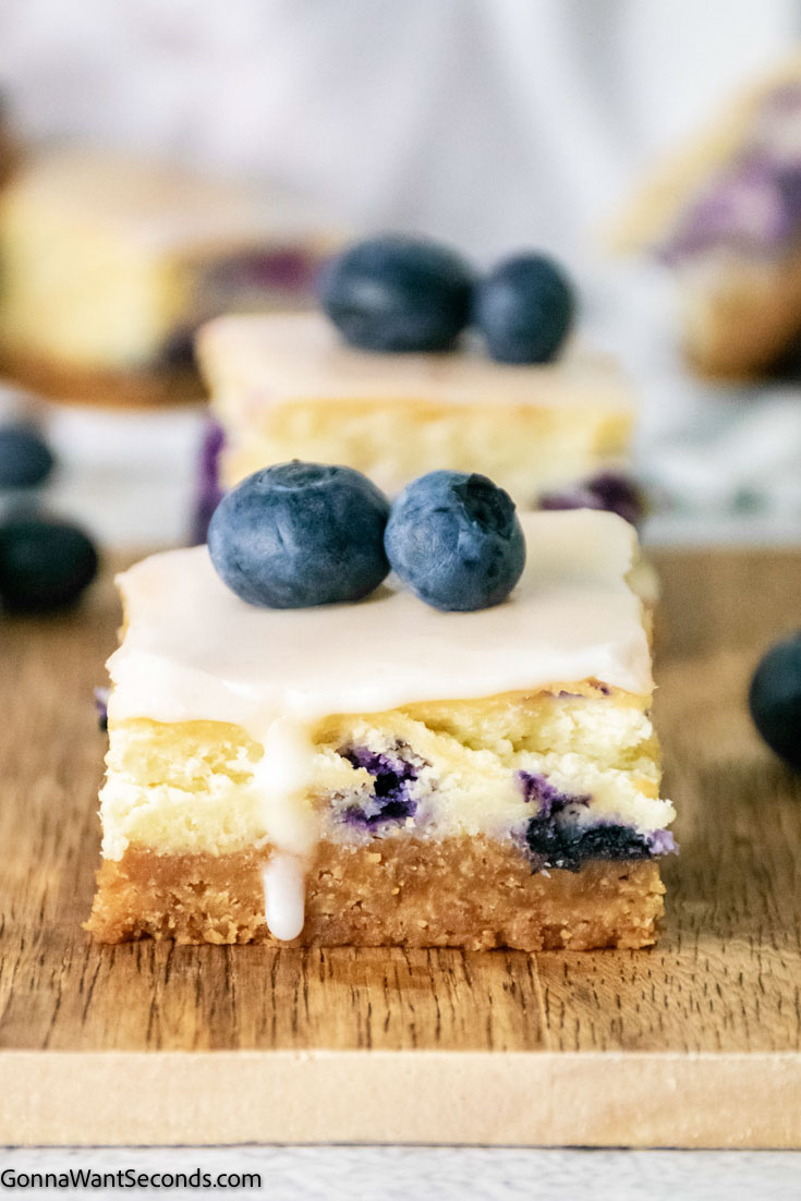 a slice of blueberry cheesecake bars topped with fresh blueberries 