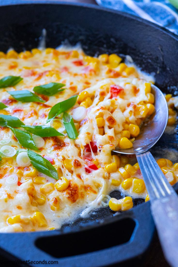 Scooping corn cheese in a cast iron skillet