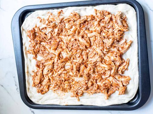 How to make sheet pan BBQ chicken pizza , spreading chicken on the dough