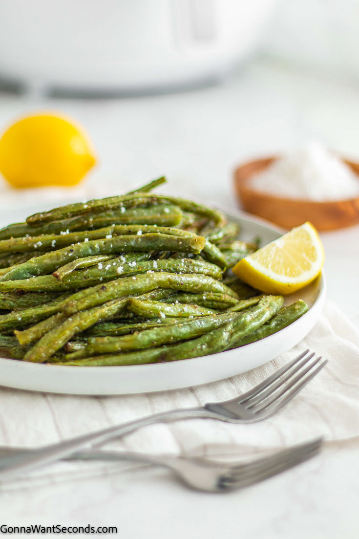 green beans in air fryer with lime wedge on the side, on a plate