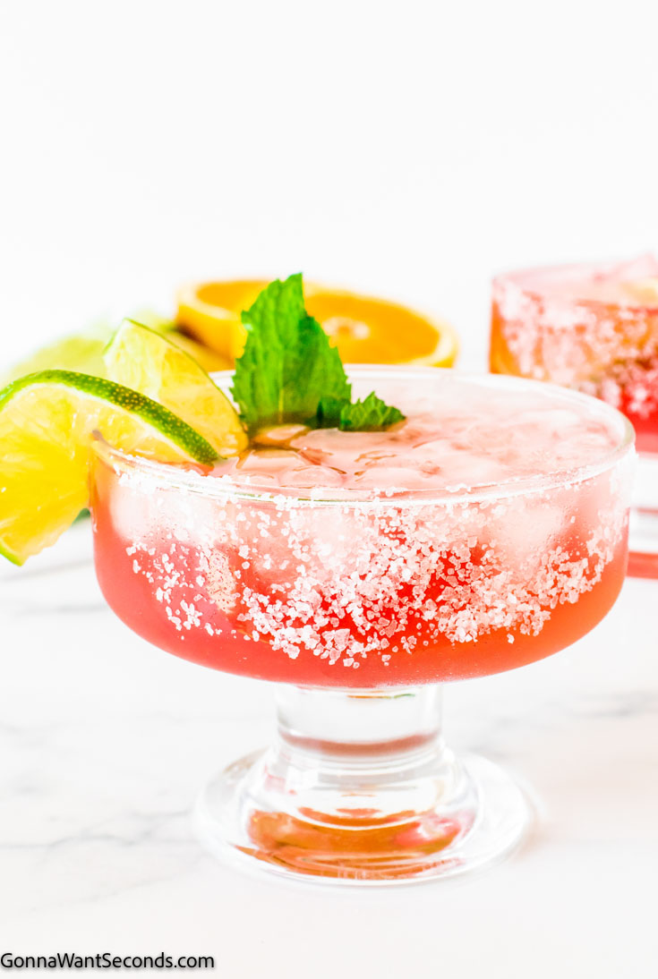 Pink Margarita garnished with lime wedges and mint, in a short stem cocktail glass