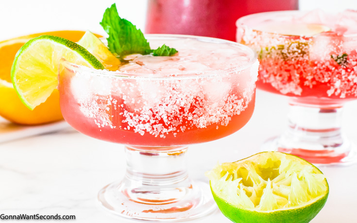 frozen pink margarita garnished with lime wedges and mint, in a short stem cocktail glass