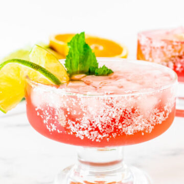 Pink Margarita garnished with lime wedges and mint, in a short stem cocktail glass