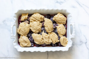 how to make easy blackberry cobbler, add cake topping on top of the fruit filling