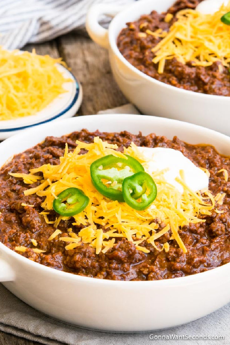 award winning texas chili recipe topped with shredded cheese, sour cream and jalapenos, in a bowl