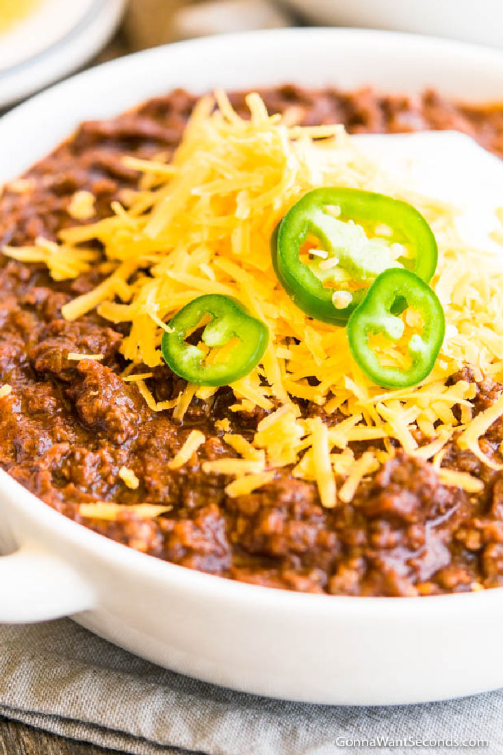 texas chili with ground beef recipe topped with shredded cheese, sour cream and jalapenos, in a bowl