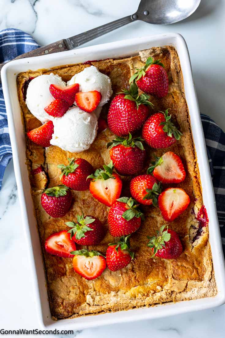 strawberry dump cake 3 ingredients topped with strawberries and vanilla ice cream in a baking dish