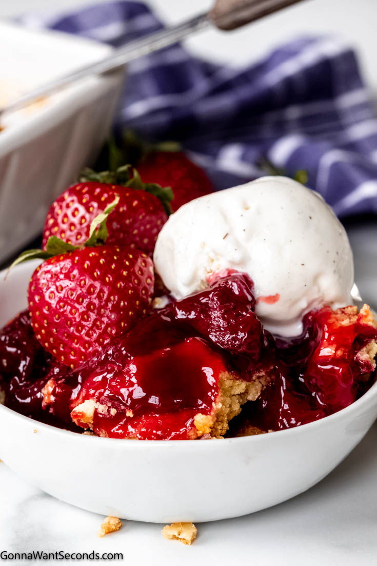 strawberry dump cake with pie filling topped with fresh strawberries and vanilla ice cream