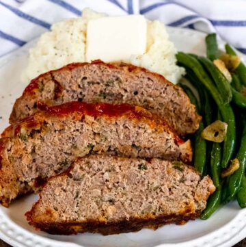Slices of traditional meatloaf recipe with mashed potato and green beans on a plate