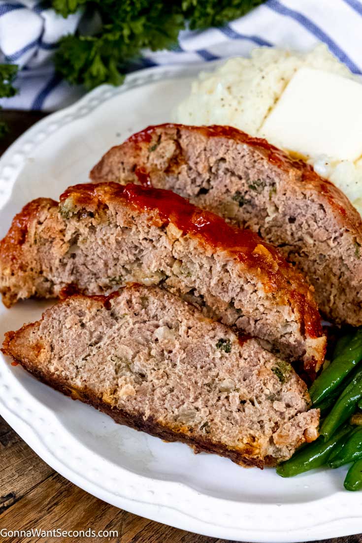 Slices of traditional meatloaf recipe with ketchup glaze with mashed potato and green beans on a plate