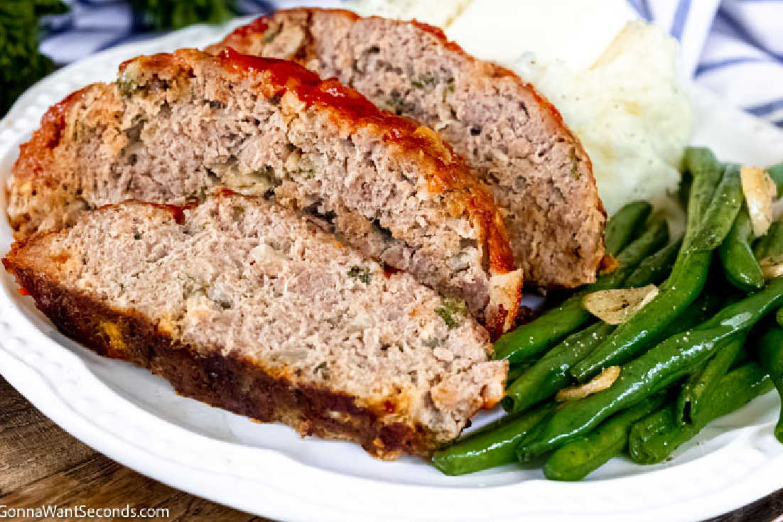 Slices of classic meatloaf with mashed potato and green beans on a plate