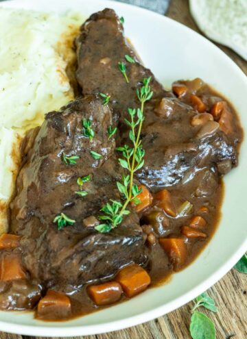 boneless beef short ribs with sauce garnished with fresh thyme sprigs and mashed potatoes on the side