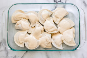 Step 2 how to make pierogi casserole recipe with frozen pierogi , spoon half of the alfredo sauce