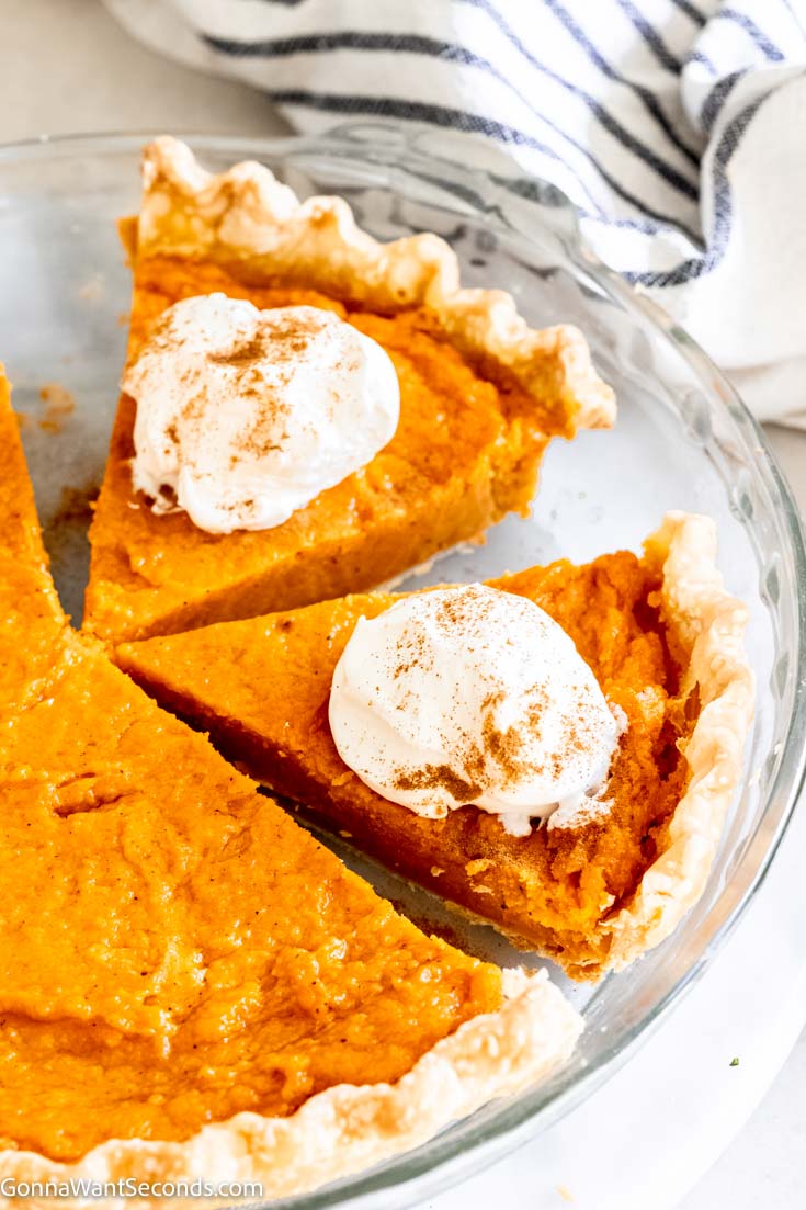 Whole classic sweet potato pie with 2 slices of pie with whipped cream on top