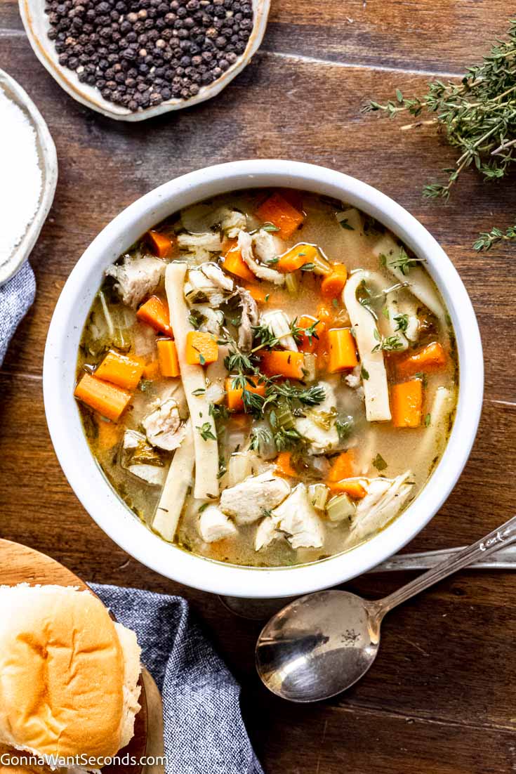 turkey carcass soup in a bowl together with herbs, spices, and bread on a wooden table