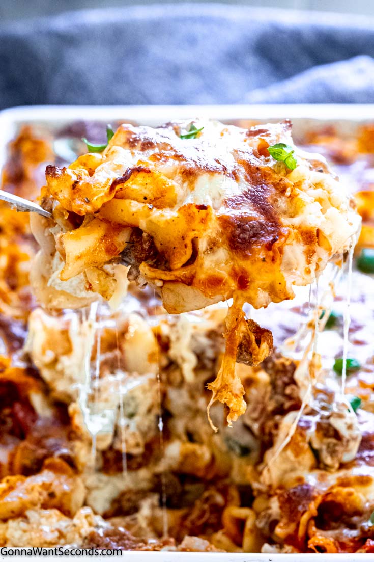 Scooping lazy lasagna casserole with cheese strings drips from a baking dish