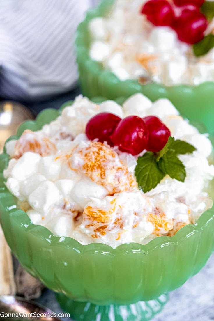 My mom often made this 5 cup salad for the family. It has tangy citrus, sweet mandarin oranges, fluffy marshmallow, shredded coconut, and sour cream. #5cupsalad #fivecupsalad old fashioned 5 cup salad with cherries on top in a green sherbet glass