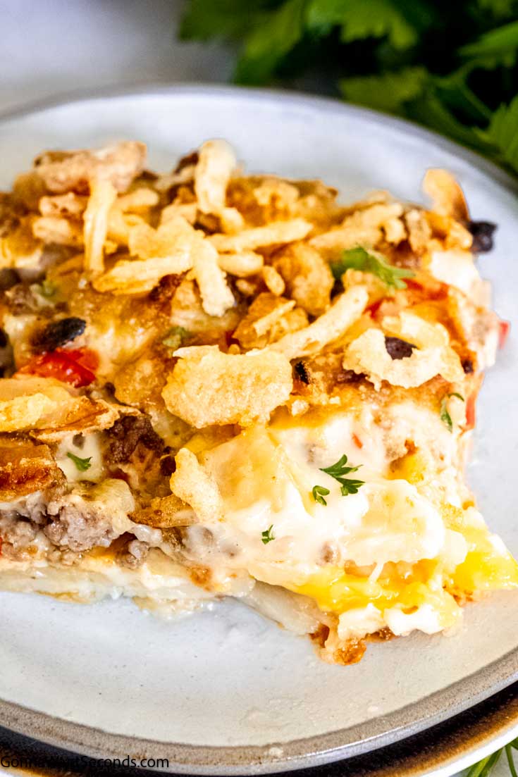 This comforting and hearty hobo casserole uses the layering of potatoes, cheese, spiced meat, and veggies, topped with a creamy savory gravy. #hobocasserole #beefpotatocasserole A serving of hobo hamburger casserole on a plate