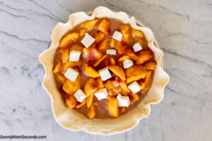 Step 6 how to make peach pie, Remove the pie crust from the fridge and pour the peach mixture into the pan. Dot with small cubes of butter.