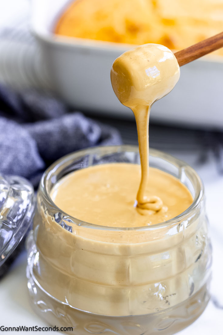 Whipped honey has a toffee-like texture that's soft-spreadable, making it a new way to enjoy cornbread, biscuits, and even plain toast! #whippedhoney #honey A wooden honey dipper is pouring whipped honey into a glass honey jar