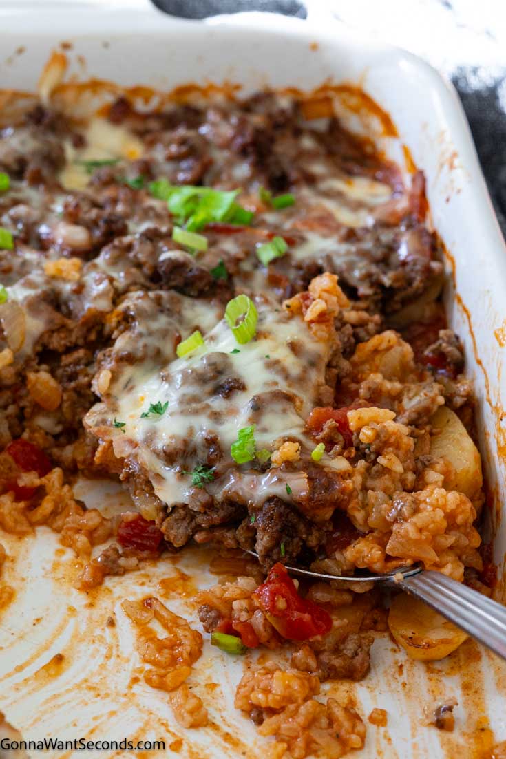This shipwreck casserole is layered with rice, beef, potatoes, bacon, tomatoes, all covered with a beefed-up tomato soup broth and topped with cheese. #casseroles #shipwreckcasserole scooped a portion of shipwreck casserole with potatoes