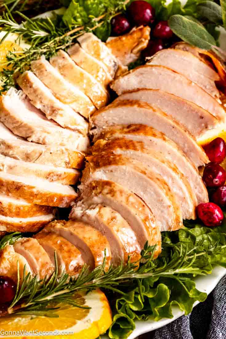 Our crockpot turkey breast is the easiest way to prepare a turkey breast. It's moist and tender, there's no need to brine the turkey to keep it moist.#crockpotturkey #turkeybreast slow cooker turkey breast sliced on a platter with fresh herbs, fresh cranberries, and orange slices