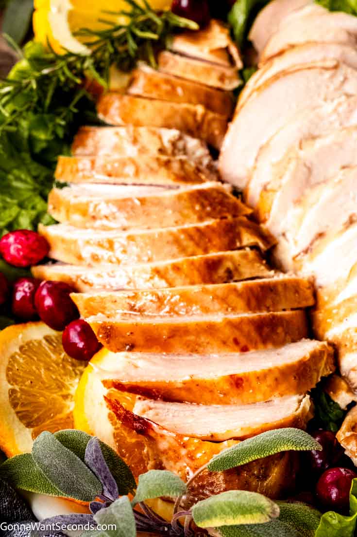 Our crockpot turkey breast is the easiest way to prepare a turkey breast. It's moist and tender, there's no need to brine the turkey to keep it moist.#crockpotturkey #turkeybreast crockpot turkey breast boneless sliced on a platter with fresh herbs, fresh cranberries, and orange slices