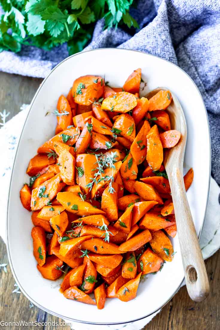 Soft, sweet, and buttery candied carrots with a rich brown sugar glaze. Easy oven recipe that’s perfect for holidays or weeknights. #candiedcarrots #carrots candied roasted carrots in a serving platter with wooden spoon