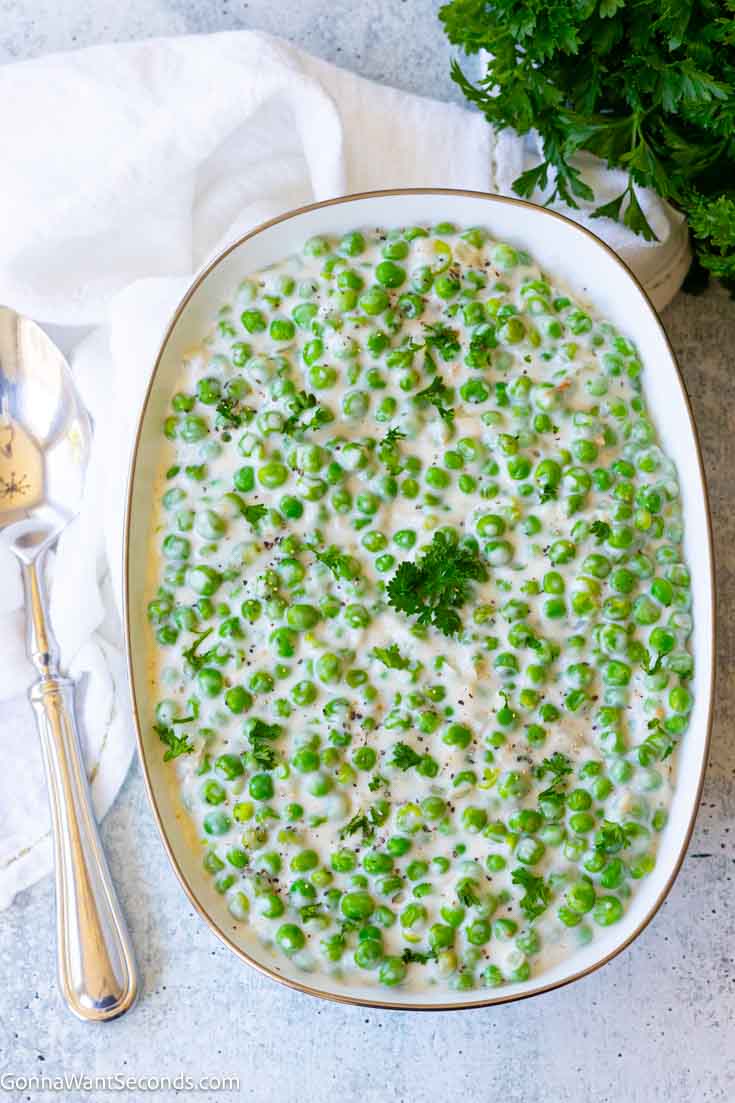 Creamed peas is the answer to boring plain veggies. With just a few basic ingredients and 15 minutes, it’s the perfect holiday side dish so save this recipe! #creamedpeas creamed peas on a serving platter