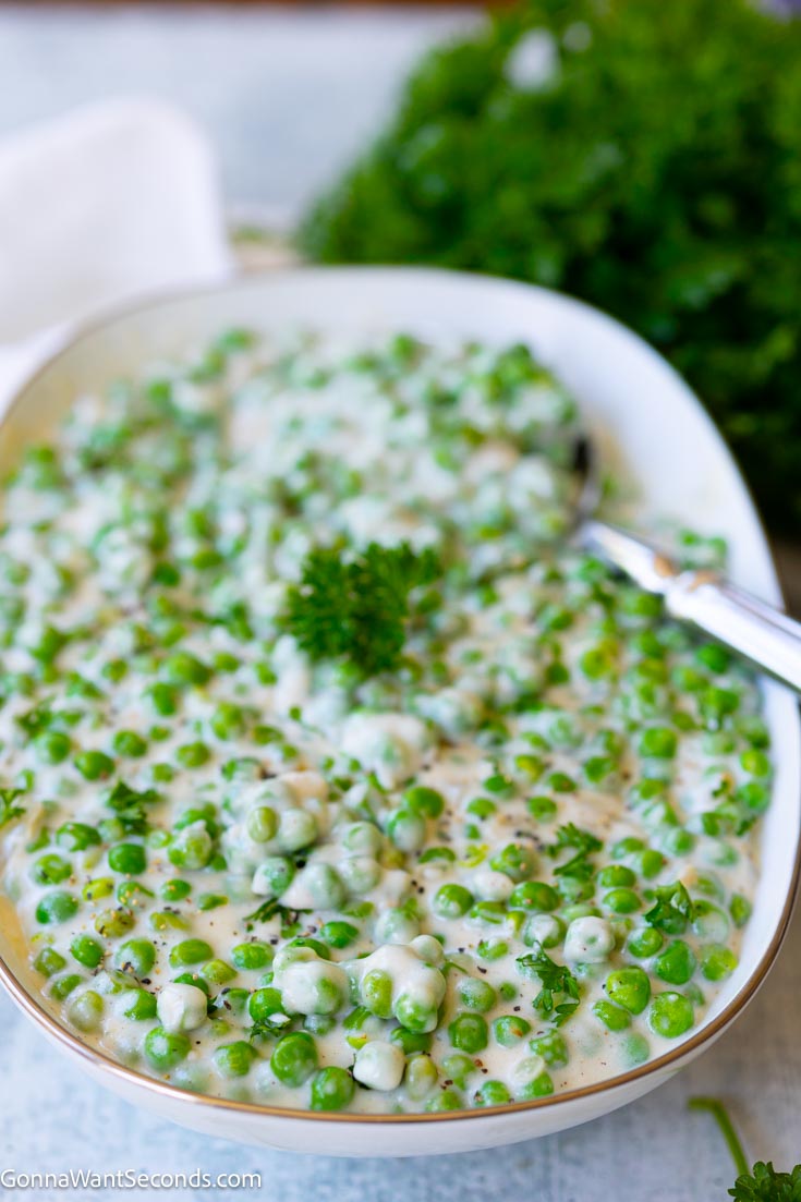 Creamed peas is the answer to boring plain veggies. With just a few basic ingredients and 15 minutes, it’s the perfect holiday side dish so save this recipe! #creamedpeas creamed green peas on a serving platter