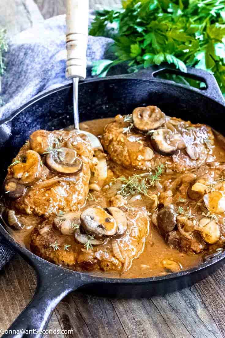 Our salisbury steak is melt-in-your-mouth tender, perfectly seasoned, then smothered in mushroom onion gravy. Just like Grandma's! #hamburgersteak #salisburysteak easy salisbury steak recipe with brown gravy in a cast iron skillet