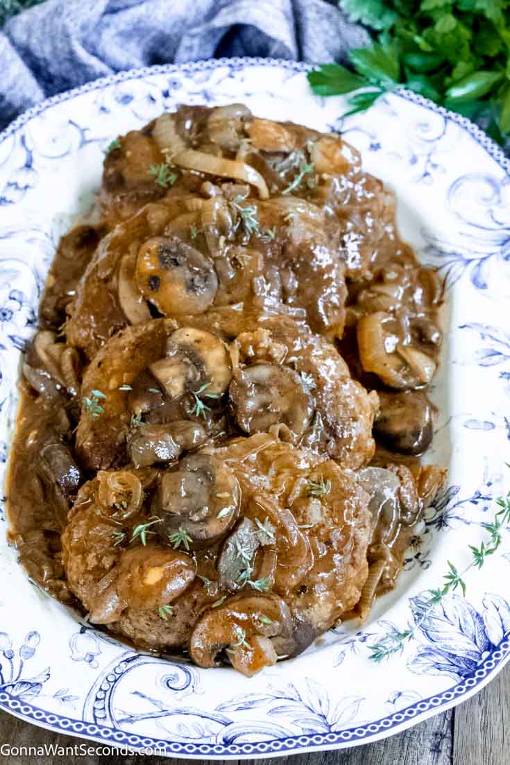 Our salisbury steak is melt-in-your-mouth tender, perfectly seasoned, then smothered in mushroom onion gravy. Just like Grandma's! #hamburgersteak #salisburysteak salisbury steak with onion gravy in a serving dish