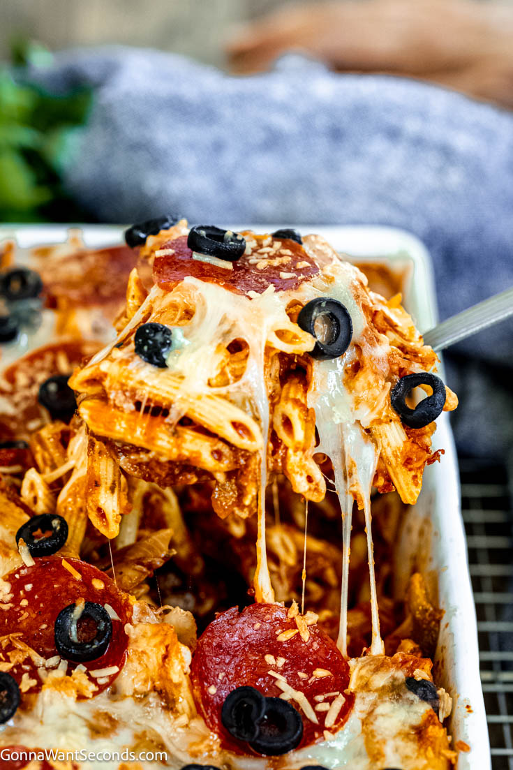 Our deliciously hearty pizza casserole will be kids of all ages will race to the dinner table when this is on the menu! Ooey-gooey, cheese YUM! #pizzacasserole #pizzapastacasserole scooping pizza pasta casserole
