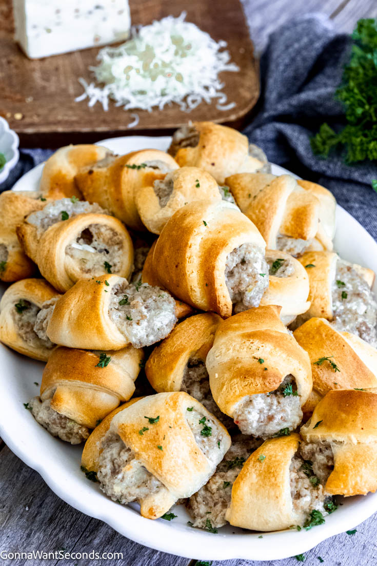If you are craving an appetizer that is fast and easy to make, this sausage cream cheese crescents fill the bill! These savory bites are baked crescent rolls filled with a cheesy sausage filling. #appetizers #sausagecreamcheesecrescents a pile of sausage cream cheese crescents on a serving platter