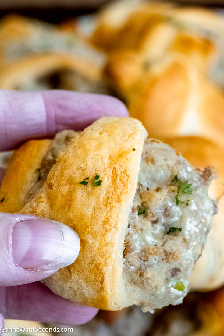If you are craving an appetizer that is fast and easy to make, this sausage cream cheese crescents fill the bill! These savory bites are baked crescent rolls filled with a cheesy sausage filling. #appetizers #sausagecreamcheesecrescents holding a piece of sausage cream cheese crescents