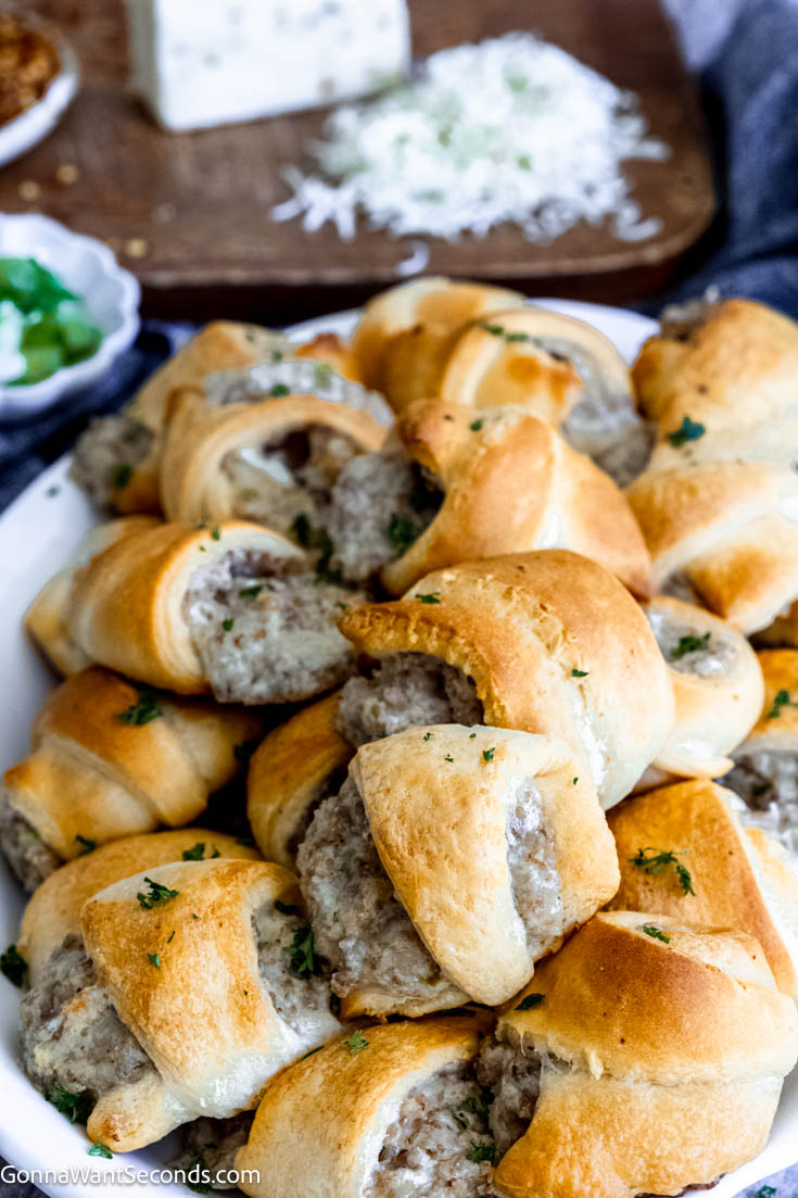 If you are craving an appetizer that is fast and easy to make, this sausage cream cheese crescents fill the bill! These savory bites are baked crescent rolls filled with a cheesy sausage filling. #appetizers #sausagecreamcheesecrescents a pile of sausage cream cheese crescents on a serving platter