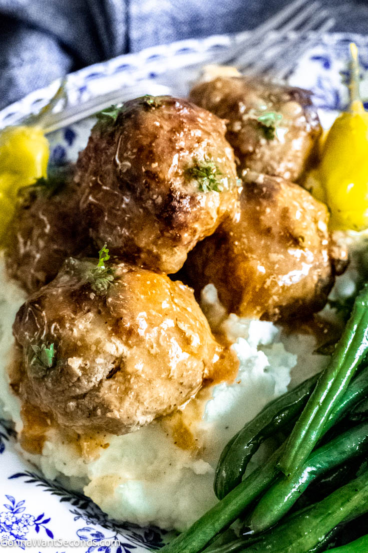 Our Crockpot Mississippi meatballs follow the delicious Mississippi recipes tradition. Moist tender meatballs in a brothy gravy flavored with pepperoncini, ranch dressing and au jus gravy. #crockpotmeatballs #mississippimeatballs Mississippi meatballs with homemade meatballs on top of mashed potatoes with green beans on the side