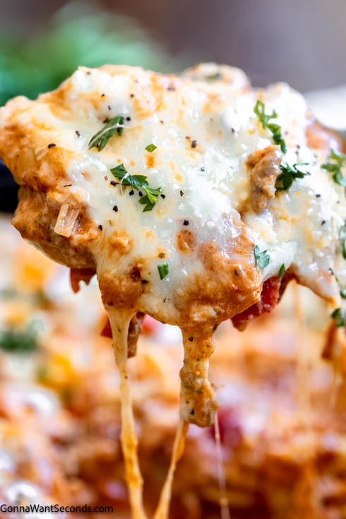 This quick and heart-warming Tortellini casserole is loaded with onions, bell peppers, Italian sausage, and tortellini in creamy tomato sauce. #tortellinicasserole #pastacasserole a scoop of tortellini casserole with sausage with string of melty cheese falling on the side