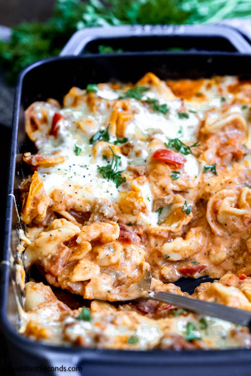 This quick and heart-warming Tortellini casserole is loaded with onions, bell peppers, Italian sausage, and tortellini in creamy tomato sauce. #tortellinicasserole #pastacasserole scooped a portion of baked tortellini casserole
