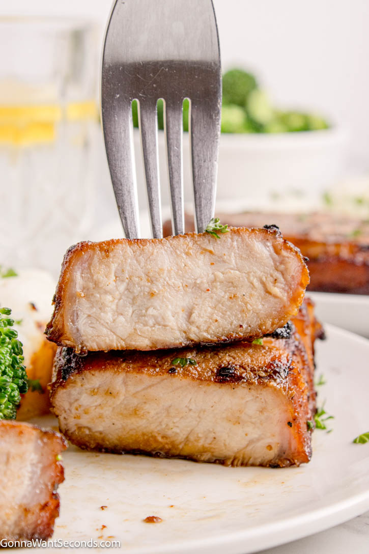 My grilled boneless pork chops is so moist and juicy. Using our quick and easy 60-minute recipe and a good grilling technique, you'll have perfect sear and tender results every time. #porkchops #grilledporkchops fork piercing a slice of grilled boneless pork chops
