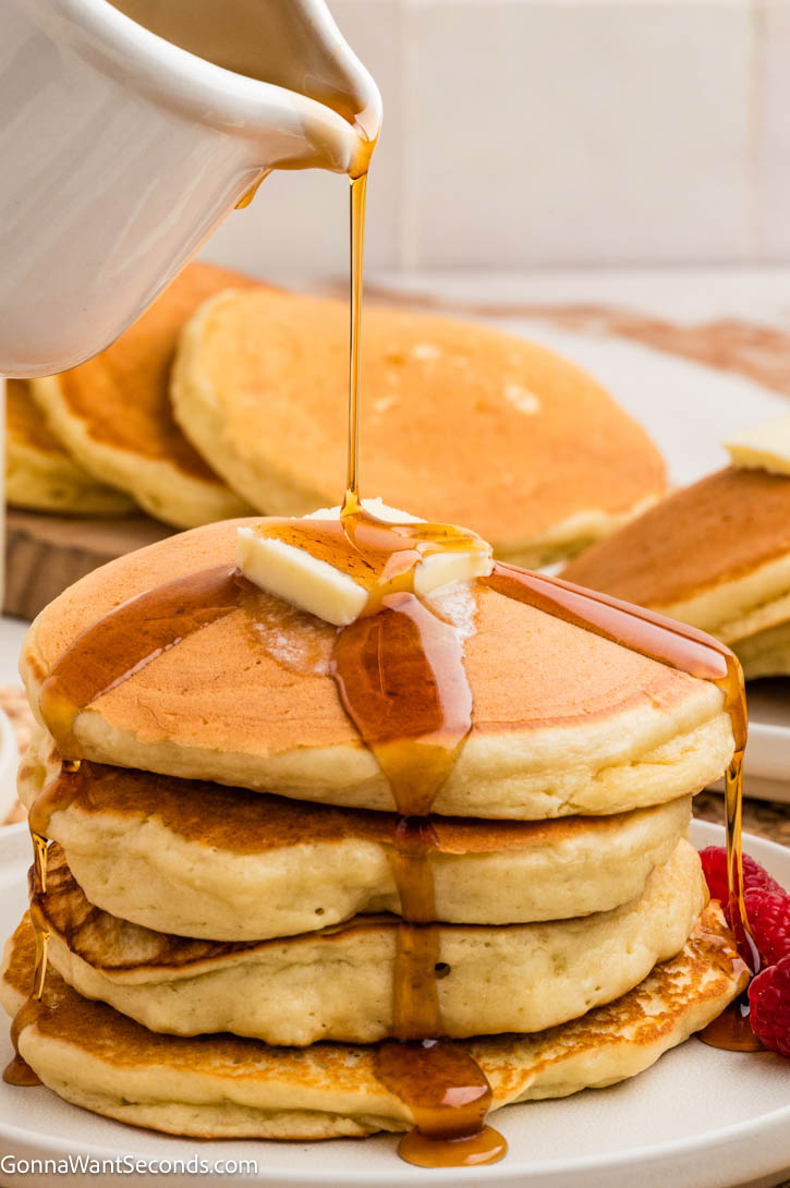 Our cream cheese pancakes are thick, fluffy, and irresistibly rich—like classic diner pancakes but with a luxurious twist. Perfect for lazy weekend mornings! #creamcheesepancakes #breakfast pouring syrup over a stack of cream cheese pancakes