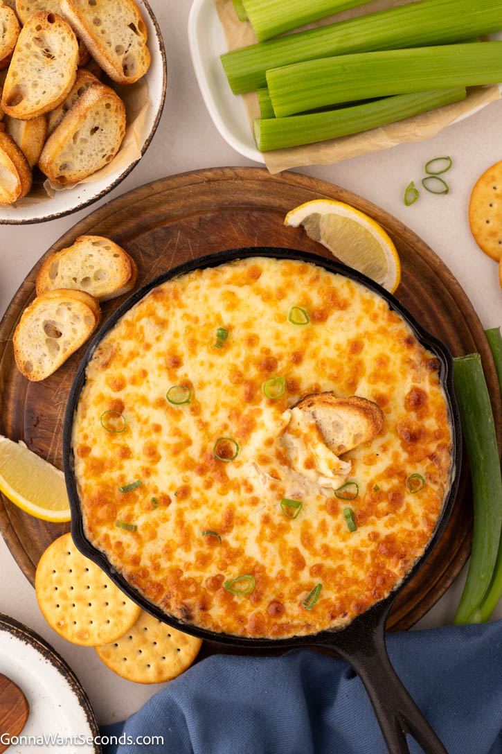 This hot crab dip is rich, creamy, and bursting with sweet crab flavor—perfect for weekends with the family, parties, or game day gatherings. #crabdip #hotcrabdip Hot Crab Dip in a cast iron skillet with crostini, crackers, and celery around
