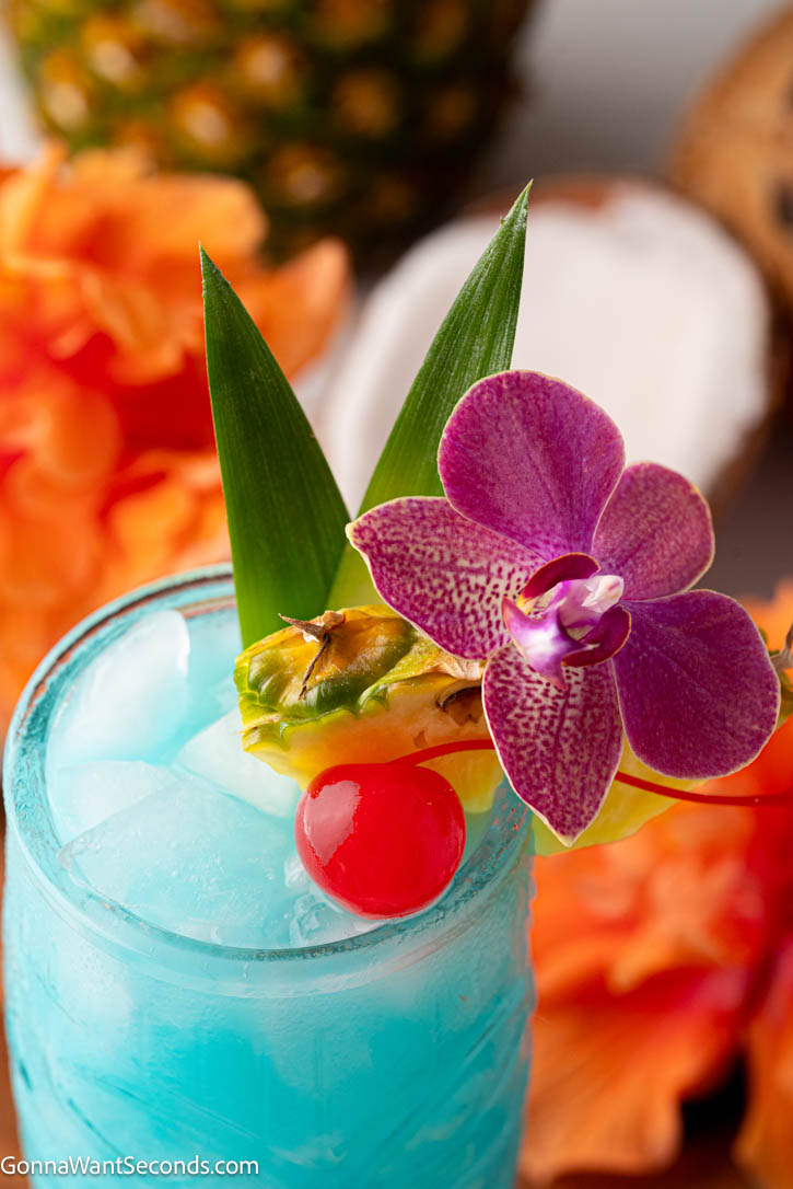 The blue Hawaiian cocktail, a tropical classic with a bright ocean-blue color, creamy coconut, and sweet pineapple flavor, is a delightful vacation in a glass. #bluehawaiiancocktails #cocktails A glass of Blue Hawaiian Cocktail with an orchid, cherry, and pineapple as garnish
